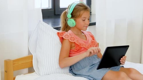 Girl uses tablet in bed with headphones