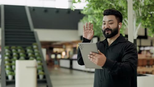 Retrato de um simpático vendedor indiano com fones de ouvido acena com a mão para o interlocutor