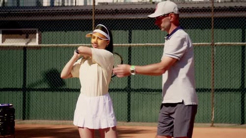 Un entraîneur de tennis se rapproche de sa salle et montre comment tenir correctement la raquette sur l'épaule pour la repousser