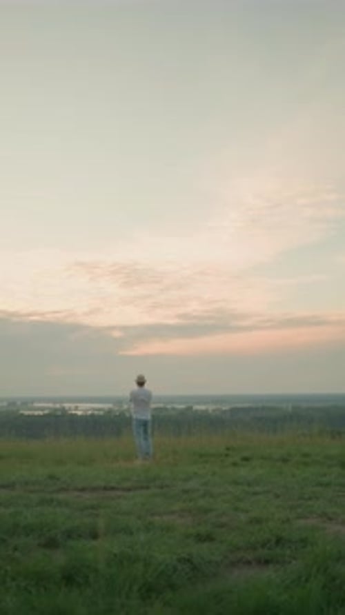 Man Contemplating at Sunset By Tranquil Lake in Grassy Field