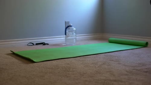Zoom in medium shot of of a green yoga mat, yoga mat strap, and water bottle to represent a home wor