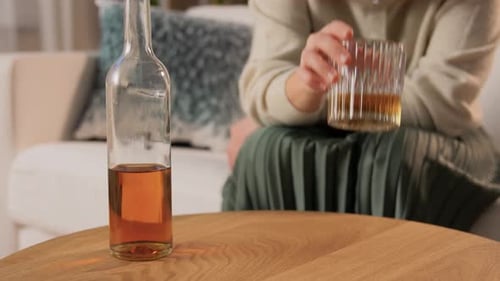 Woman near Whiskey Bottle and Glass on Table
