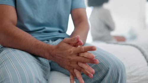 Worried Man Sits With Clasped Hands on Bed