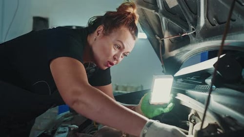 Mechanic Works Under the Hood of a Car in an Automotive Shop