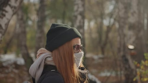 Masked White Woman in Birch Woods Guarded Profile with Sunglasses and Scarf Tense Watchful Stance