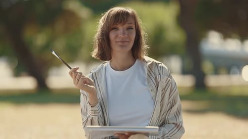 An Adult Smiling Woman Looking in the Camera Holding a Painting Brush in the Park