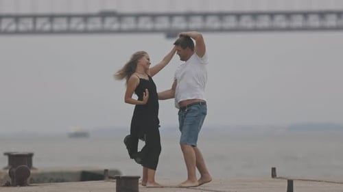 A Cute Romantic Married Couple Dancing on the Pier with a Bridge on the Background in Overcast
