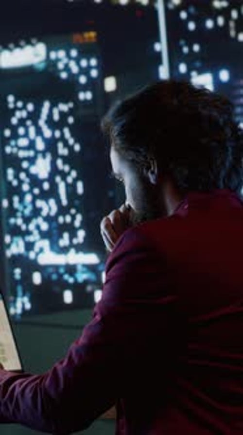Adult Works at Night with Cityscape Monitor