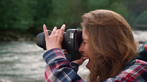 Smiling woman takes photos with digital camera riverside