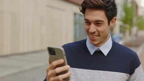 Young Man Smiling and Using Smartphone Outdoors