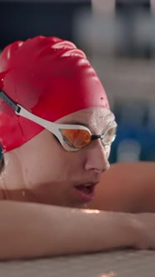 Focused Swimmer in Red Cap Resting at the Pool Edge After Practice Water Droplets on Face and