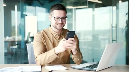 Businessman is using smartphone sitting at workplace in business office. Entrepreneur reads