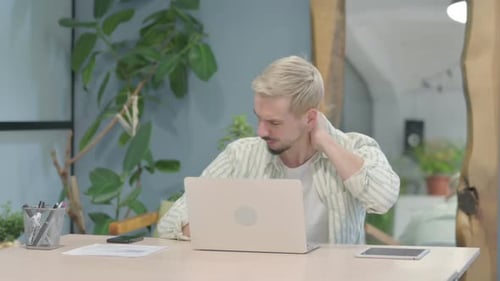 Young Adult Massaging Stiff Neck While Working on Laptop