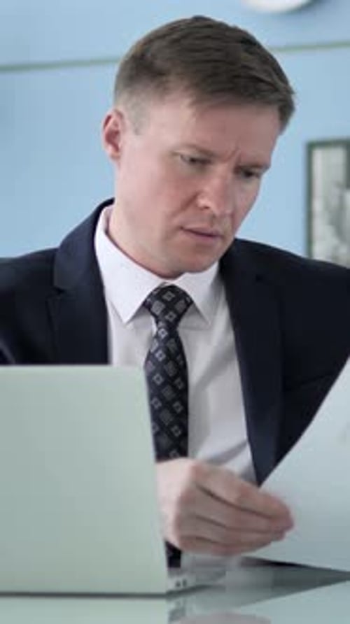 Man Reviews Documents at Desk with Laptop
