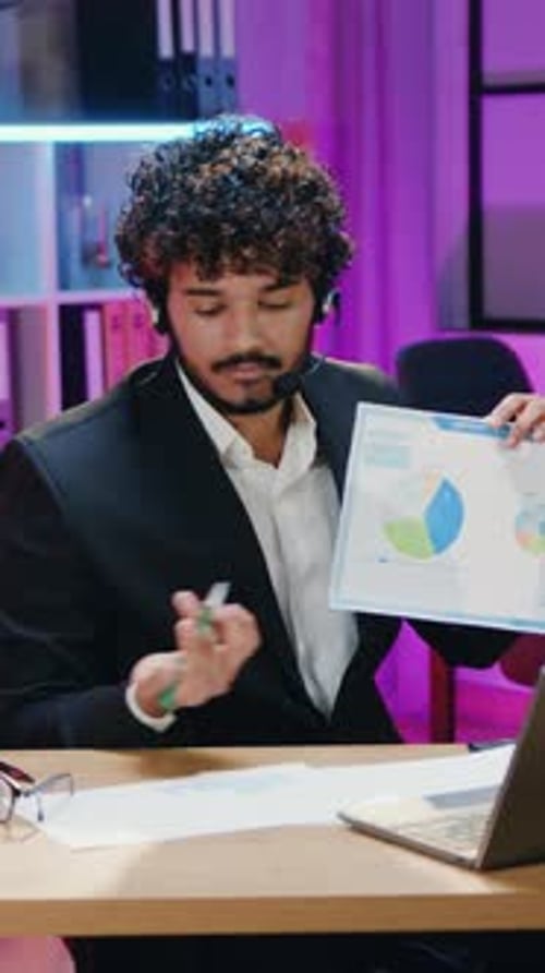 Attractive Man Office Manager in Wireless Headphones Discussing Infographics with Business Partners