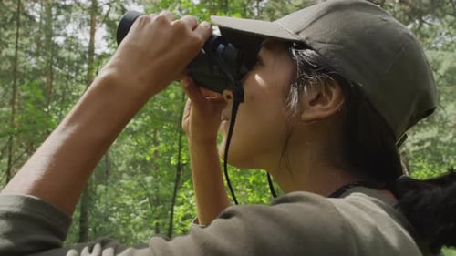 Woman looks through binoculars in a green forest