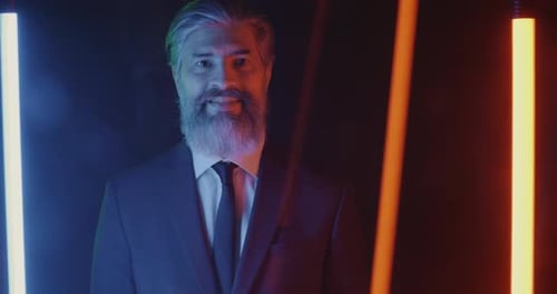 Portrait of Successful Entrepreneur in Suit Standing Against Dark Background with Bright Neon Lamps