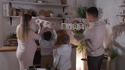 Family Hanging Happy Birthday Banner in Kitchen