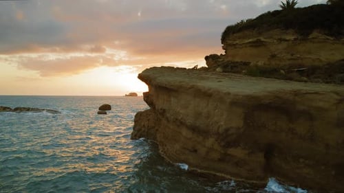 Sun setting behind a rocky cliff over the ocean with warm glowing reflections