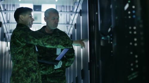 In Data Center Two Military Men Work with Open Server Rack Cabinet. One Holds Military Edition Lapt