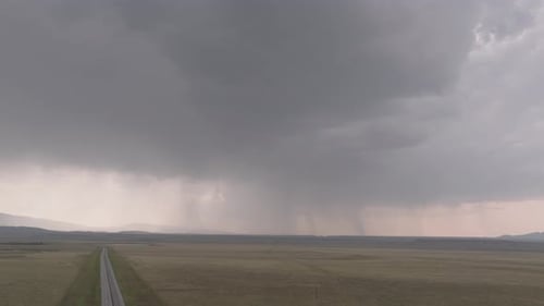 A distant storm looms over a vast open landscape with rain falling in the distance