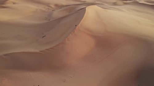 Aerial view from drone flying away from a walking young man to the top of a dune in Abu Dhabi desert