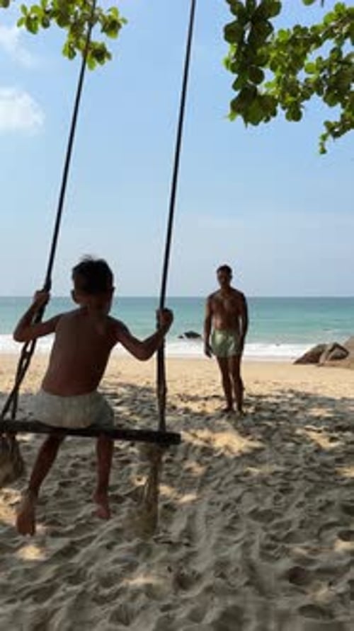 Father Pushing Son on Swing at the Beautiful Beach