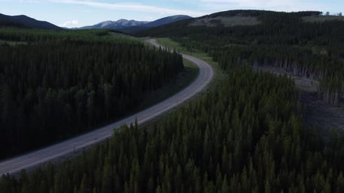 Red cars driving via mountains on highway surrounded by forest. Aerial view.