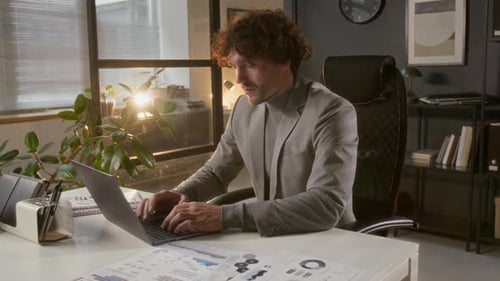 Young Male Entrepreneur Typing on Laptop at Workplace in Modern Office