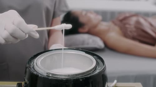 Hand of Beautician Heating Wax for Depilation Procedure