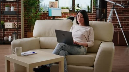 Woman Using Laptop at Home on Sofa