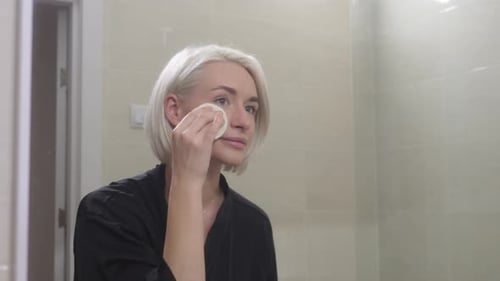 Woman Cleansing Face in Bathroom Mirror