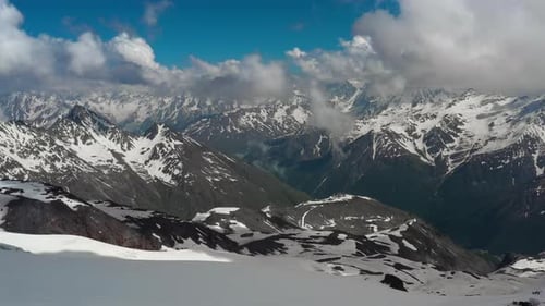 Luftflug durch Bergwolken über wunderschöne schneebedeckte Gipfel von Bergen und Gletschern.