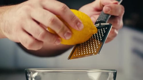 Makro-Nahaufnahme eines professionellen Kochs mit Zitrone und Reibe, bei dem Zitronenschale für Limonadensalat gerieben werden