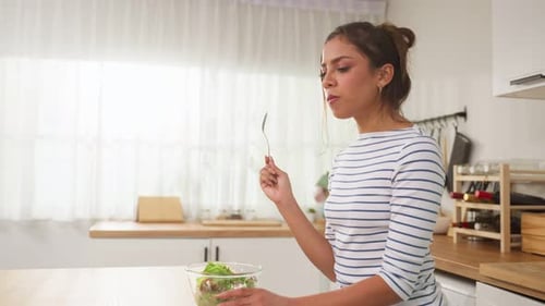 Caucasian young woman eating healthy green salad in kitchen at home.