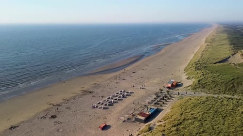 A beautiful aerial view of a sandy beach with rows of beach huts, people relaxing by the shore