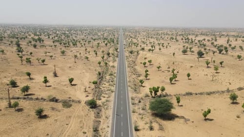 Aerial drone shot capturing a lone vehicle moving along an empty highway surrounded by desert dunes.