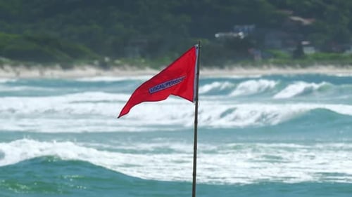 Red Flag Blows on Tropical Beach with Waves