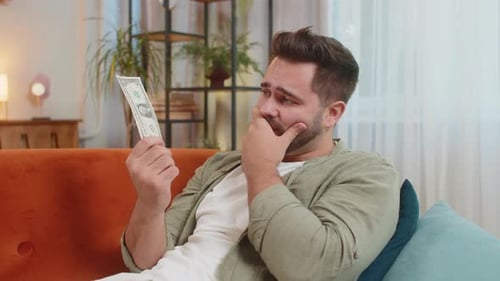 Man Counting Money on Couch Looks Disappointed