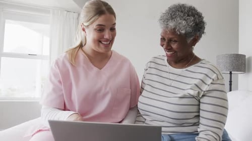 Caucasian female nurse and senior african american woman using laptop, copy space, slow motion