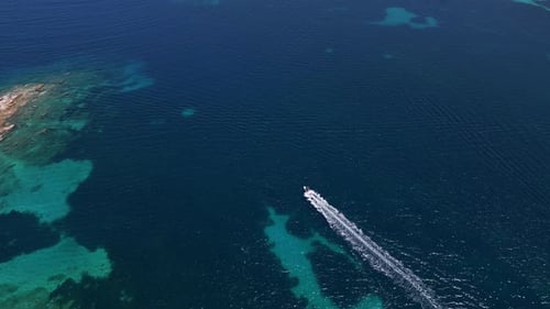 Aerial View of a Lone Boat Speeding Across the Calm Dark Blue Ocean Leaving a Trail of White Waves