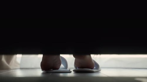 Woman Puts on White Slippers Getting Out of Bed on the Floor in a Hotel Room The Guest Puts Her Feet