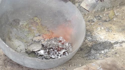Molten lead in a crucible with visible flames and fumes, in an industrial setting, top down view