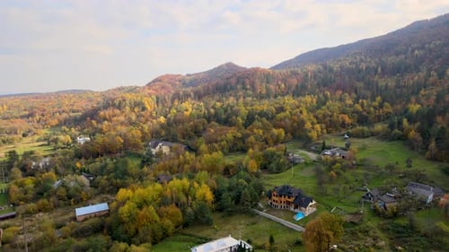 Aerial View of a Rural Village with Small Houses Between Autumn Mountain Hills Covered with Yellow