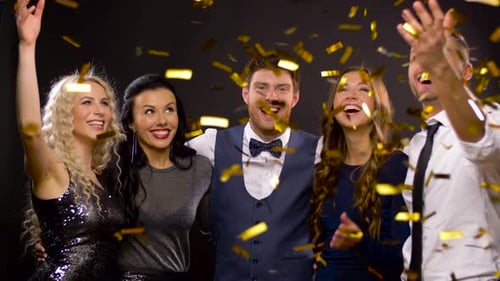 Glückliche Freunde feiern Silvester unter goldenem Konfetti, das auf einer Party eingegossen wird