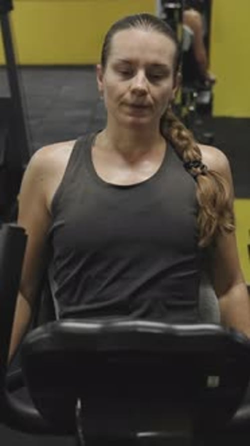 Vertical video. Young Woman with Long Hair Tied in a Braid Exercising on a Stationary Bike.