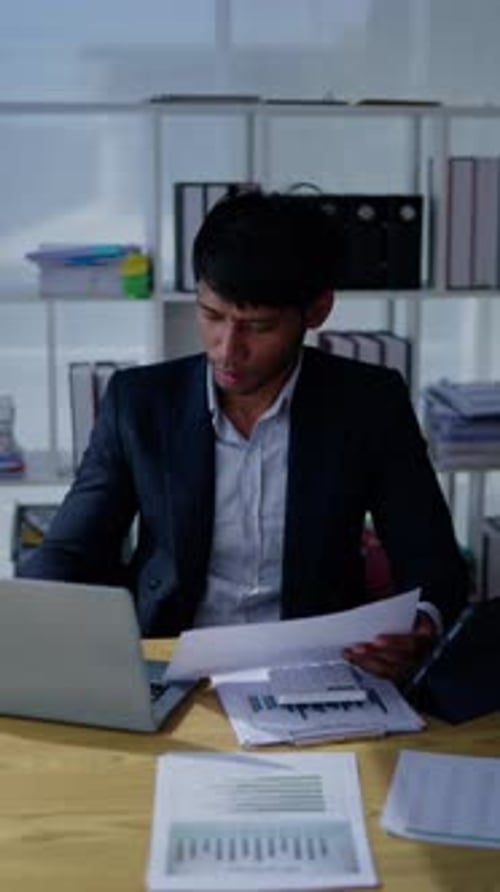 Focused Young Adult Reviews Financial Documents at Desk