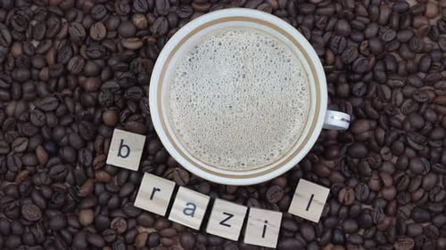 Top View of a Cup of Coffee on a Background of Coffee Beans with the Inscription Brazil