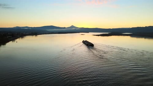Drone panning to the left, watching over a large ship laying in the middle of a big lake during sunr