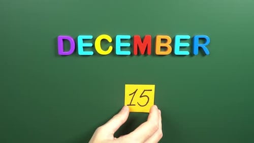 Hand sticking a sticker 15 December calendar day on school board. 15 date of December. Fifteenth